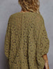 A woman viewed from behind wearing a loose, olive green crochet cardigan with an intricate openwork pattern, set against a neutral gray background.