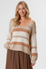 A woman wearing a cream and tan striped knit sweater with a V-neck and long sleeves, paired with a brown skirt, against a solid beige background.