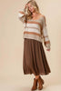 A woman wearing a beige and brown striped knit sweater with white denim shorts, posed against a solid beige background.