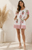 Woman wearing a white dress with floral patterns standing in a bright room.